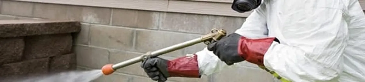 Pest control technician applying exterior insect treatment along a home foundation in Irvine, CA