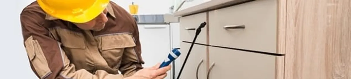 Roach exterminator applying treatment under kitchen cabinets in Irvine, CA