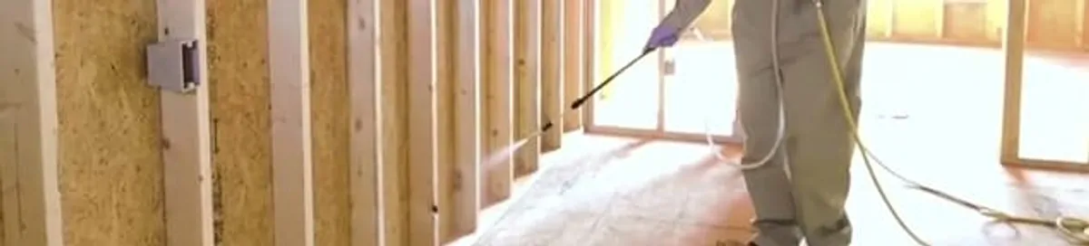 Termite treatment technician applying spray along framing and unfinished walls in Irvine, CA